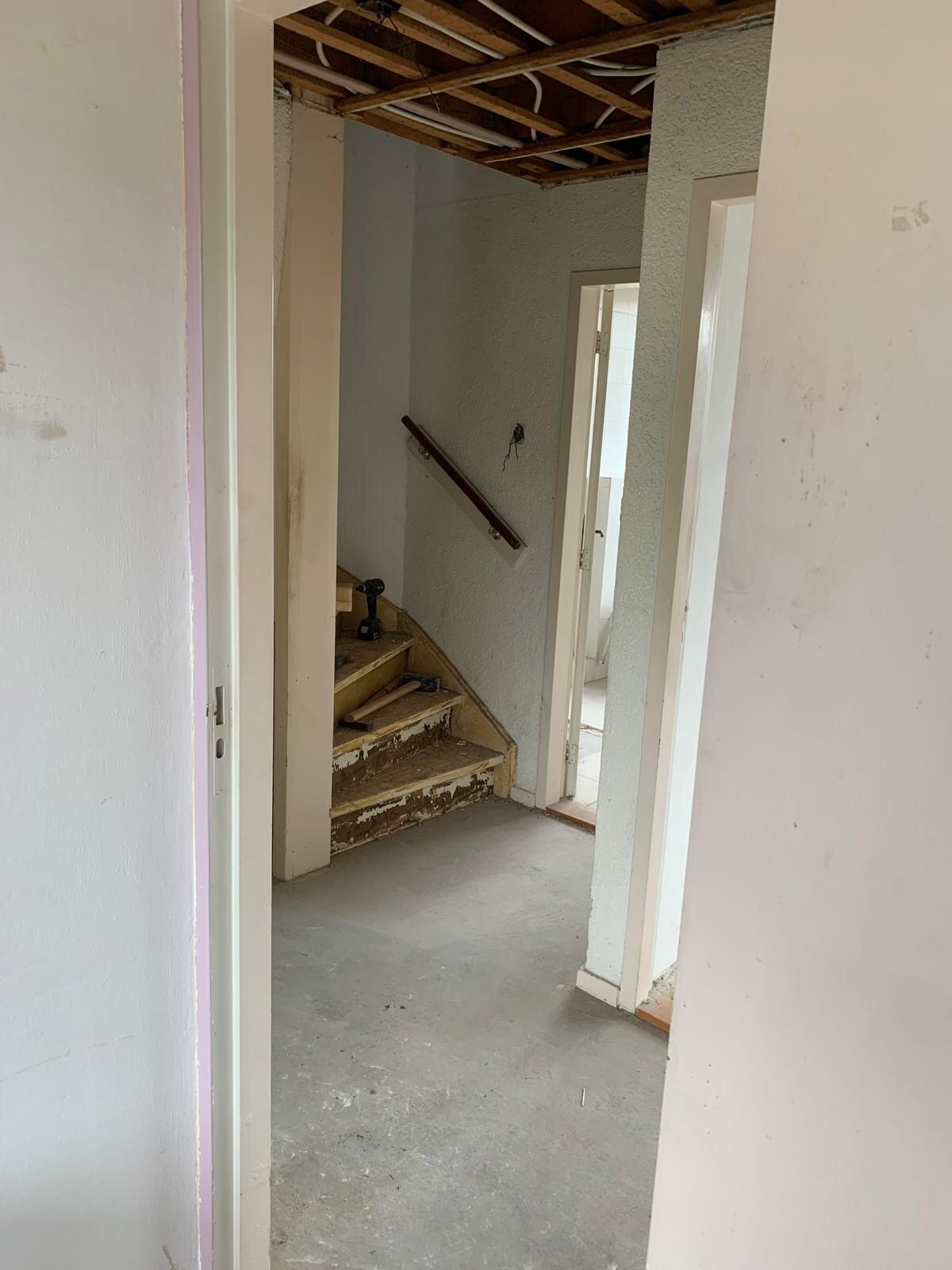 Dezelfde overloop gestript: kale treden, open plafond met balken en strakke wanden