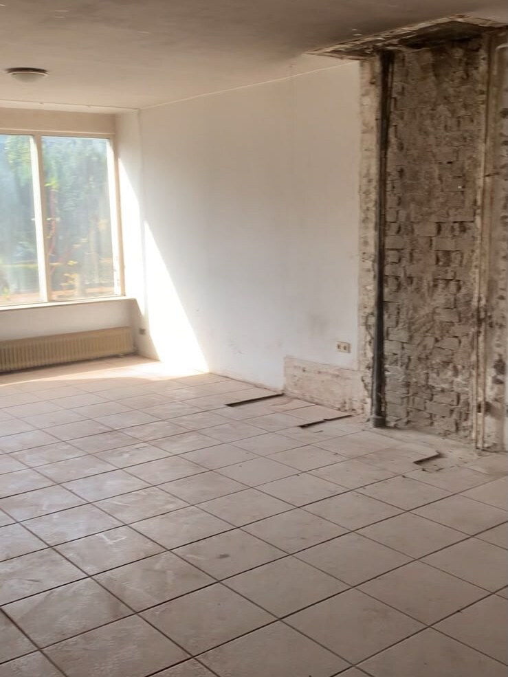 Dezelfde woonkamer leeg en gestript, met het metselwerk van de schouw in het zicht