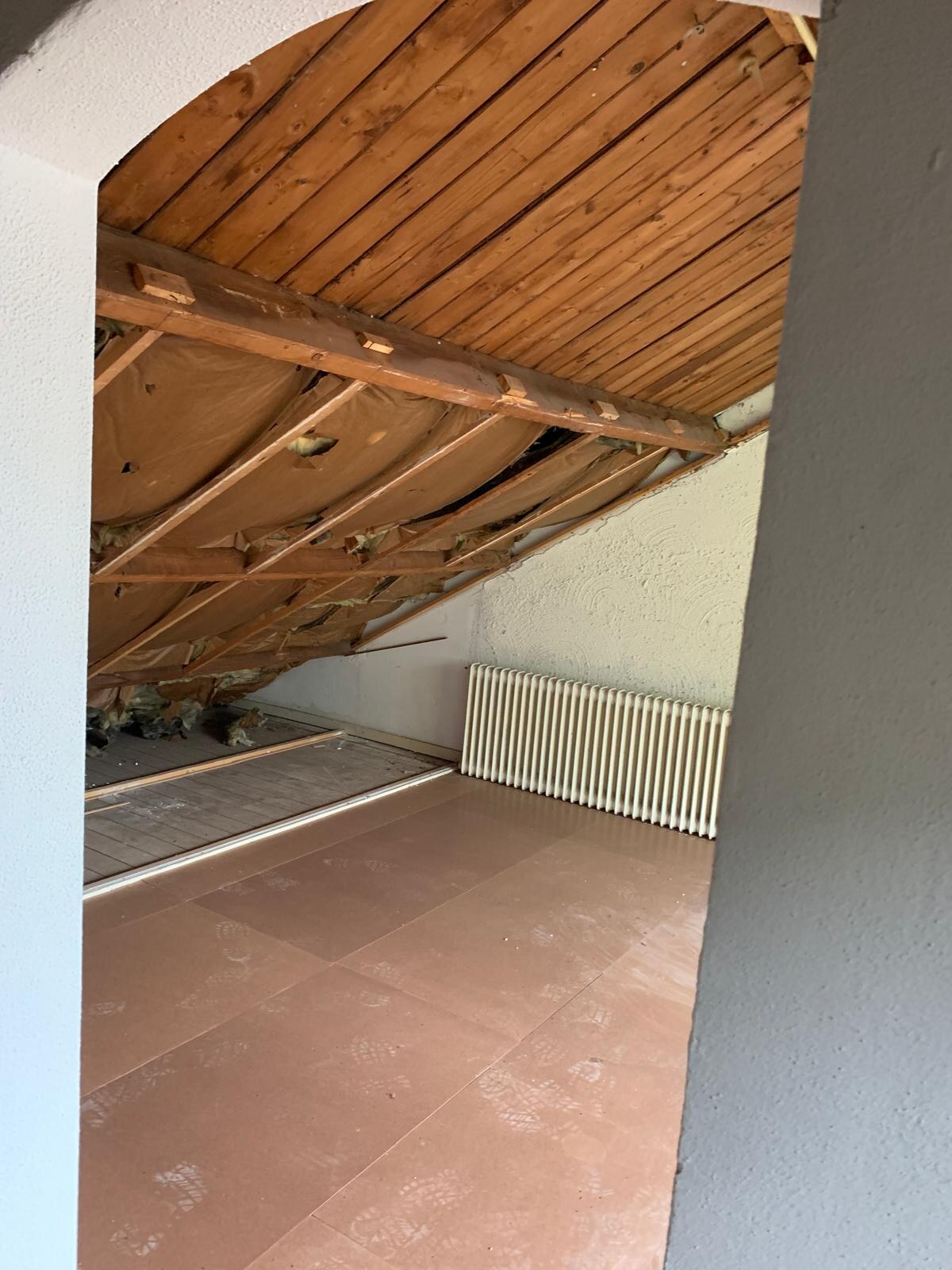 Dezelfde zolder gestript tot op de houten kapconstructie, met kale vloer en radiator